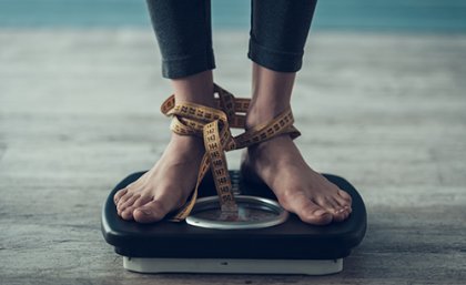 Woman's feet standing on scales with tape measure wrapped around her ankles